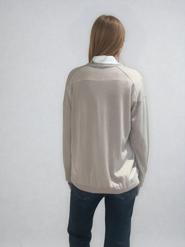 Pull manches longues col V coloris beige en 100% mérinos extra fine. Les manches se terminent par de larges côtes qui permettent de porter un chemisier avec facilité. Finitions larges côtes  également sur le bas. Le pull est fendu sur les côtés sur 10 cm. Emmanchures raglan dans le dos.
Vue dos.
