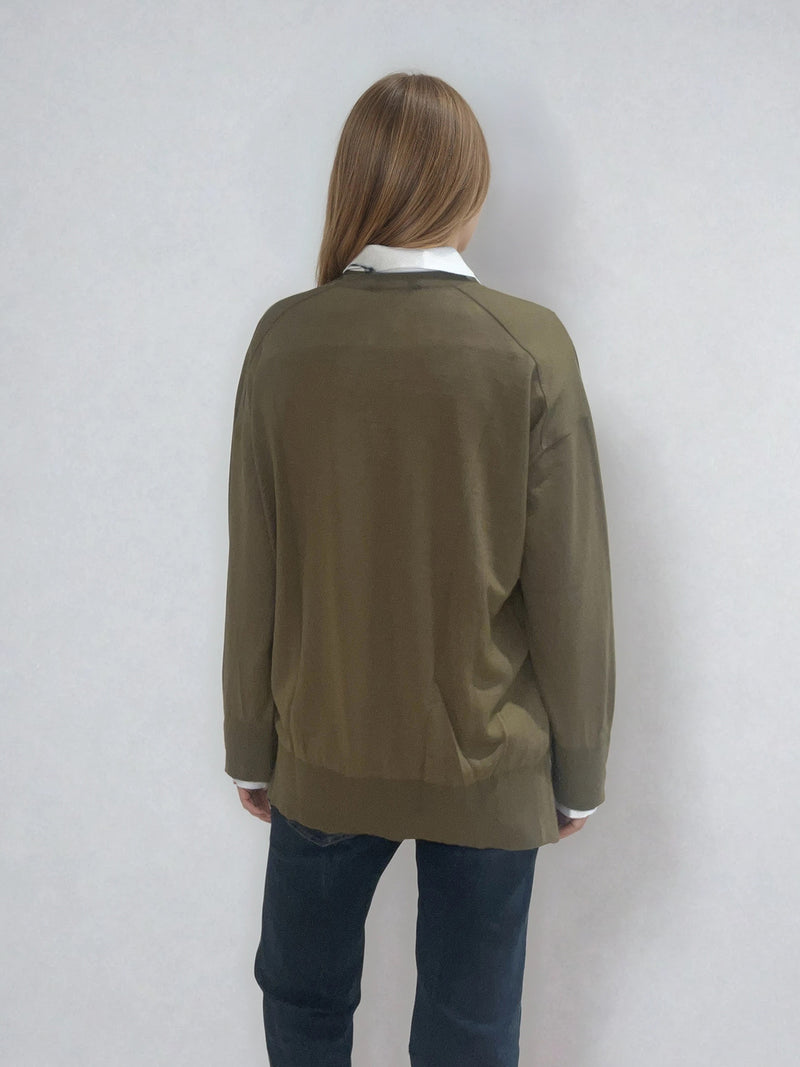 Pull manches longues col V coloris kaki en 100% mérinos extra fine.  Les manches se terminent par de larges côtes qui permettent de porter un chemisier avec facilité. Finitions larges côtes  également sur le bas. Le pull est fendu sur les côtés sur 10 cm. Emmanchures raglan dans le dos.
Vue dos.