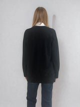 Pull manches longues col V coloris noir en 100% mérinos extra fine. Les manches se terminent par de larges côtes qui permettent de porter un chemisier avec facilité. Finitions larges côtes  également sur le bas. Le pull est fendu sur les côtés sur 10 cm. Emmanchures raglan dans le dos.
Vue dos.