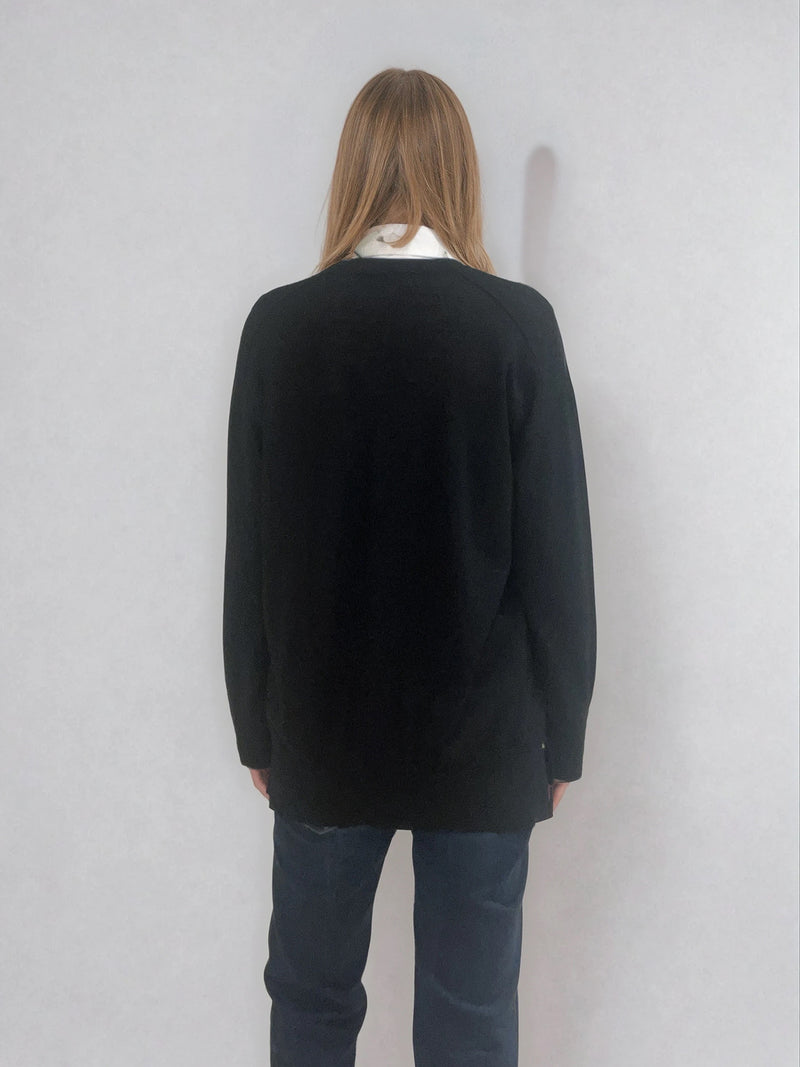 Pull manches longues col V coloris noir en 100% mérinos extra fine. Les manches se terminent par de larges côtes qui permettent de porter un chemisier avec facilité. Finitions larges côtes  également sur le bas. Le pull est fendu sur les côtés sur 10 cm. Emmanchures raglan dans le dos.
Vue dos.