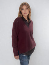 Pull manches longues coloris bordeaux avec un col V et une forme droite. Fentes asymétriques sur les côtés. Le pull est particulièrement doux, il associe du cachemire et de la soie. Finitions côtes. Vue profil.