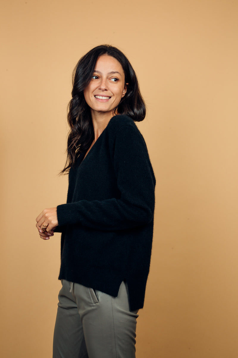 Pull manches longues coloris noir avec un col V et une forme droite. Fentes asymétriques sur les côtés. Le pull est particulièrement doux, il associe du cachemire et de la soie. Finitions côtes. Vue profil.
