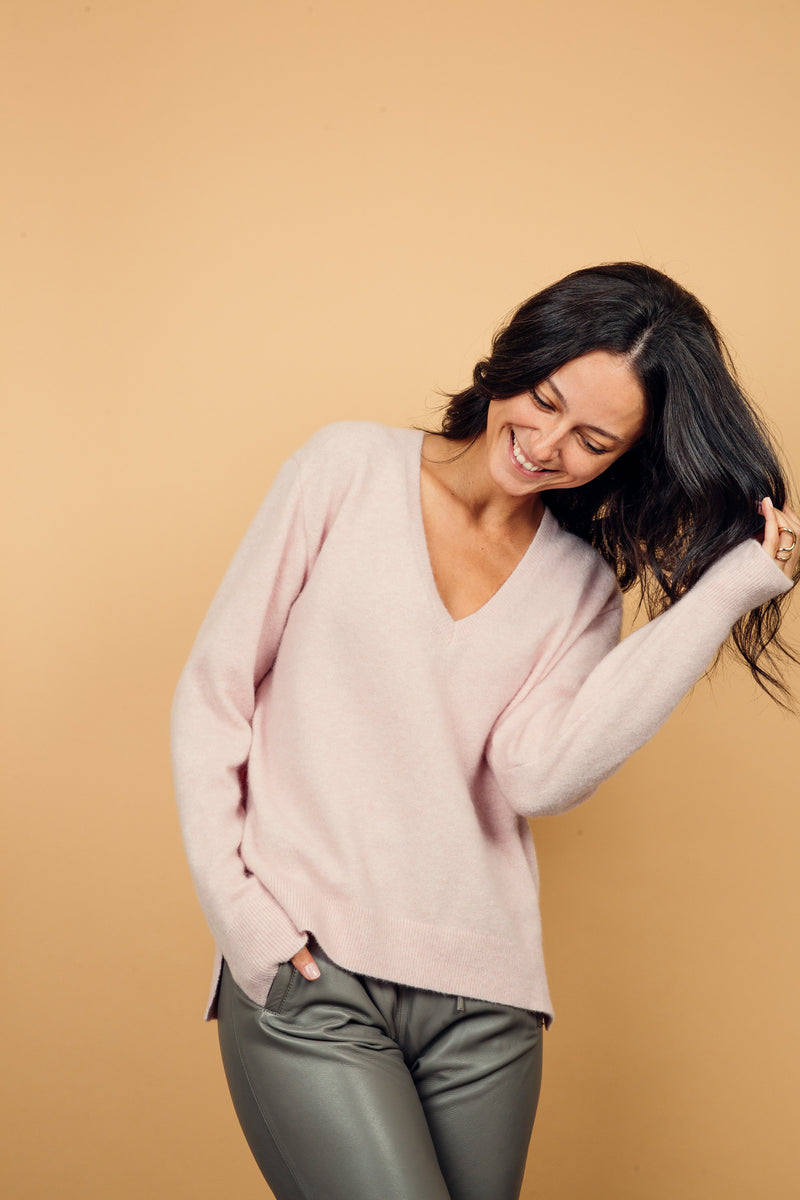 Pull manches longues coloris rose clair avec un col V et une forme droite. Fentes asymétriques sur les côtés. Le pull est particulièrement doux, il associe du cachemire et de la soie. Finitions côtes. Vue face.