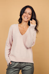 Pull manches longues coloris rose clair avec un col V et une forme droite. Fentes asymétriques sur les côtés. Le pull est particulièrement doux, il associe du cachemire et de la soie. Finitions côtes. Vue face.