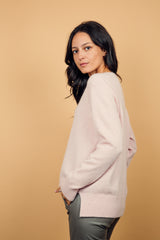 Pull manches longues coloris rose clair avec un col V et une forme droite. Fentes asymétriques sur les côtés. Le pull est particulièrement doux, il associe du cachemire et de la soie. Finitions côtes. Vue profil.