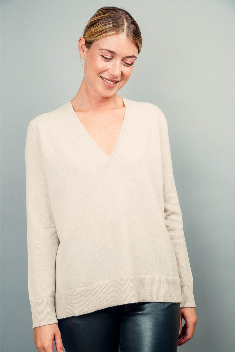 Pull manches longues coloris beige 100% cachemire, col V profond, fendu sur les côtés avec asymétrie: 10 cm dans le dos et 7 cm devant. Finitions bords côtes. 