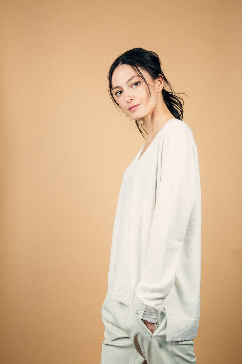 Pull manches longues coloris blanc 100% cachemire, col V profond, fendu sur les côtés avec asymétrie: 10 cm dans le dos et 7 cm devant. Finitions bords côtes. 