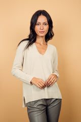 Pull manches longues coloris écru 100% cachemire, col V profond, fendu sur les côtés avec asymétrie: 10 cm dans le dos et 7 cm devant. Finitions bords côtes. 