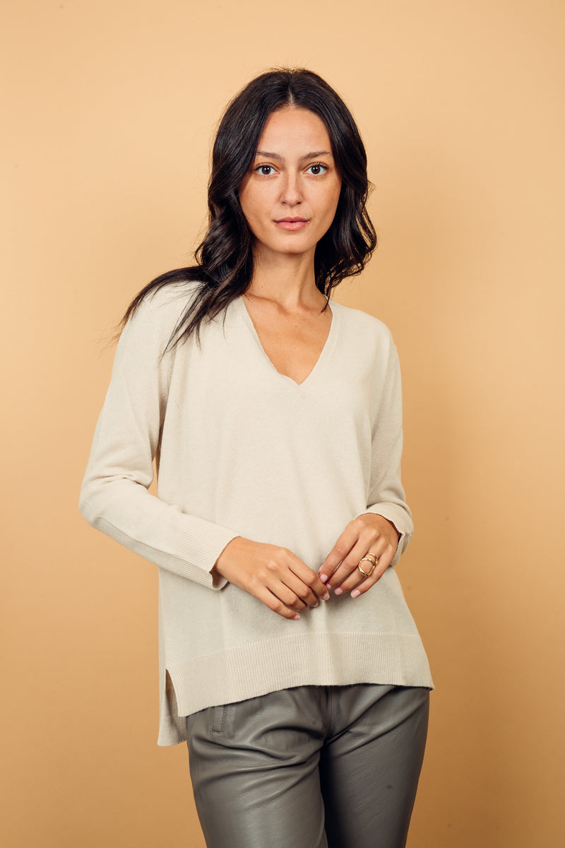 Pull manches longues coloris écru 100% cachemire, col V profond, fendu sur les côtés avec asymétrie: 10 cm dans le dos et 7 cm devant. Finitions bords côtes. 