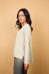 Pull manches longues coloris écru 100% cachemire, col V profond, fendu sur les côtés avec asymétrie: 10 cm dans le dos et 7 cm devant. Finitions bords côtes. 