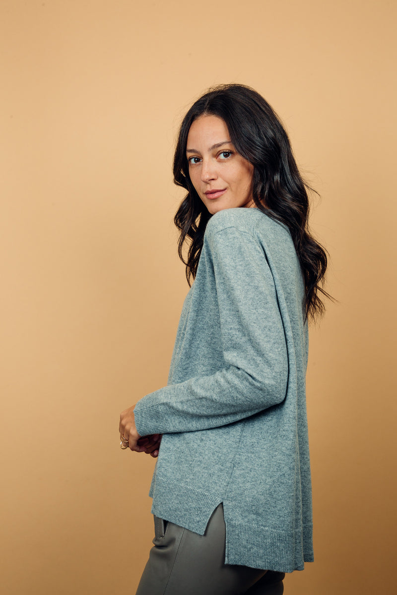 Pull manches longues coloris gris clair moyen 100% cachemire, col V profond, fendu sur les côtés avec asymétrie: 10 cm dans le dos et 7 cm devant. Finitions bords côtes. 