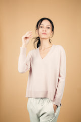 Pull manches longues coloris rose tendre 100% cachemire, col V profond, fendu sur les côtés avec asymétrie: 10 cm dans le dos et 7 cm devant. Finitions bords côtes. 