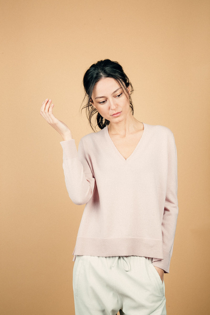 Pull manches longues coloris rose tendre 100% cachemire, col V profond, fendu sur les côtés avec asymétrie: 10 cm dans le dos et 7 cm devant. Finitions bords côtes. 