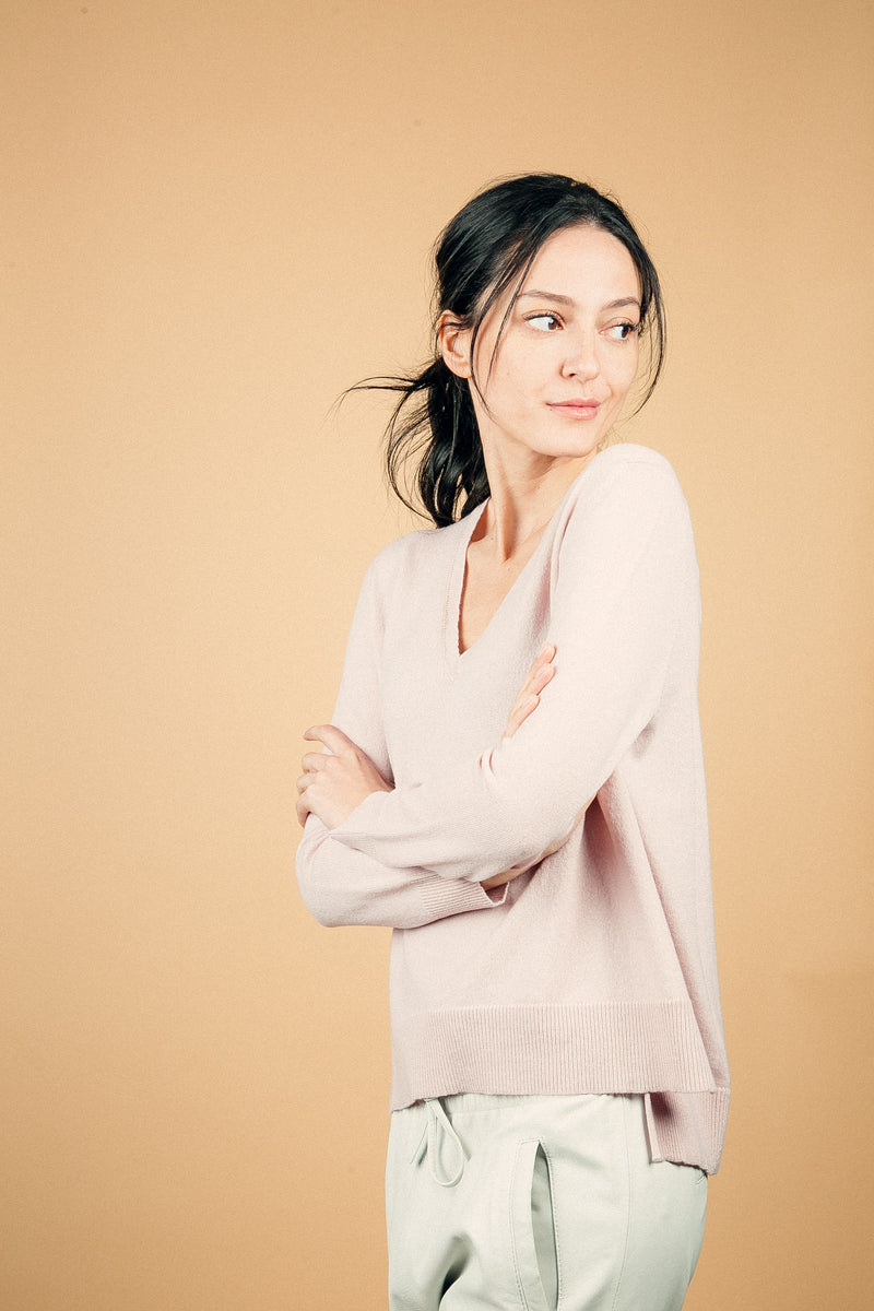 Pull manches longues coloris rose tendre 100% cachemire, col V profond, fendu sur les côtés avec asymétrie: 10 cm dans le dos et 7 cm devant. Finitions bords côtes. 