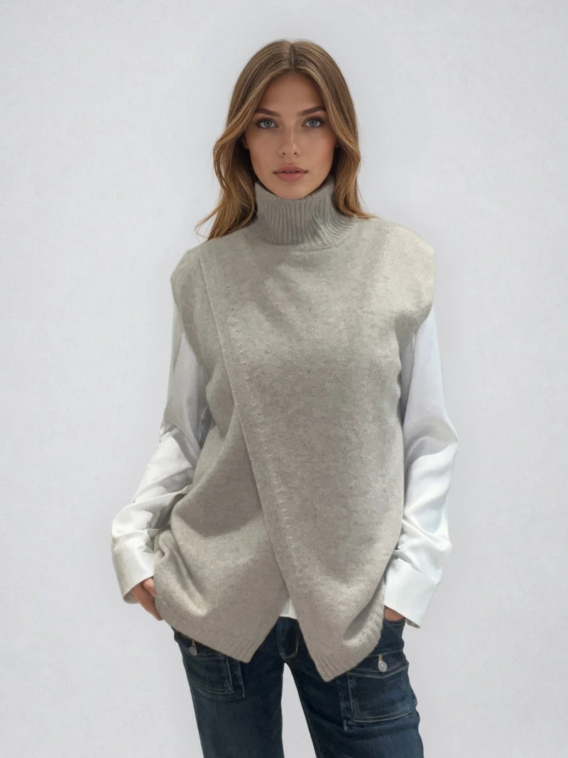 Pull sans manches taupe avec un col montant et une ouverture en diagonale sur le devant formant un croisé. A porter avec un chemisier en dessous. Coupe droite et longue.  42% cachemire, 8% soie, 50% mérinos. Vue face.