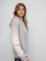Pull beige en 100% cachemire, manches longues avec une encolure ronde rehaussée d'une capuche. Coupe droite, esprit hoody, se porte assez vague. Les emmanchures sont basses. Un élégant travail de maille formé de 2 bandes termine chaque couture d'assemblage. Finitions côtes. Vue profil.