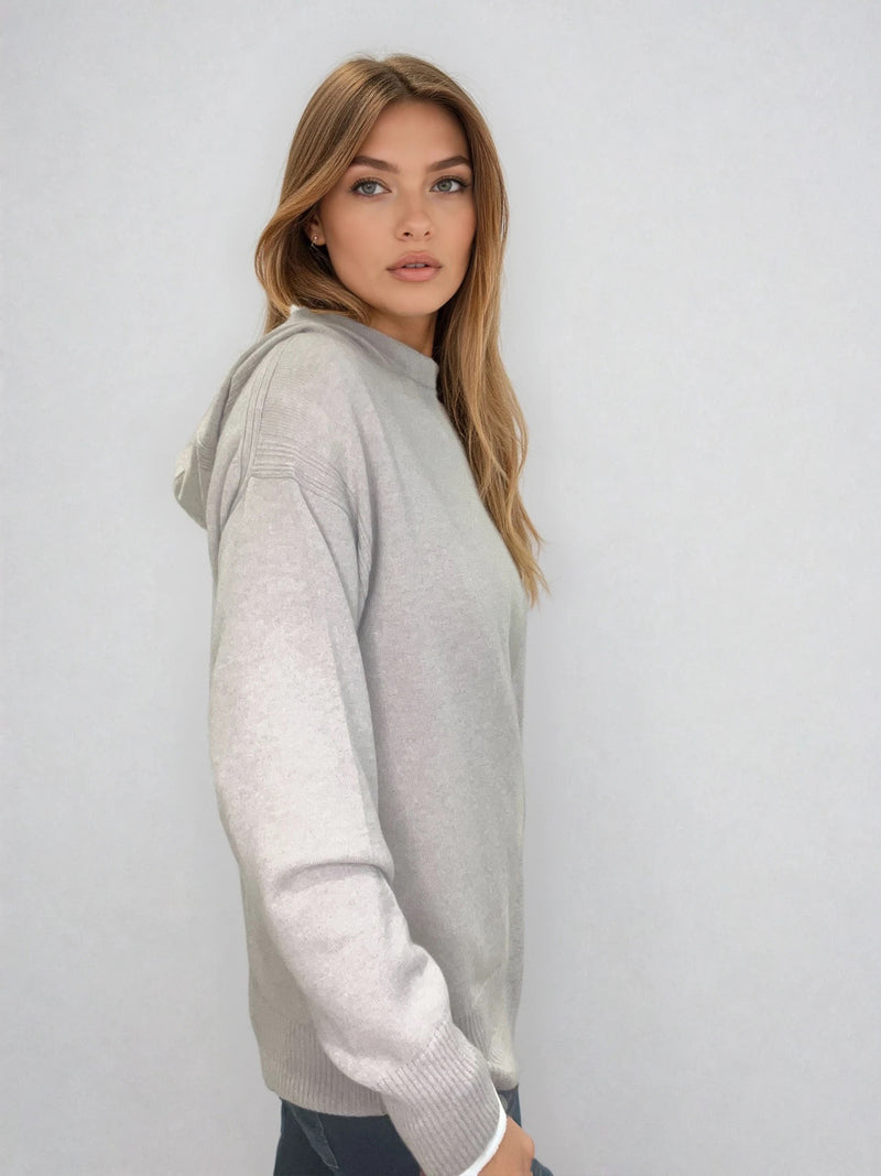 Pull beige en 100% cachemire, manches longues avec une encolure ronde rehaussée d'une capuche. Coupe droite, esprit hoody, se porte assez vague. Les emmanchures sont basses. Un élégant travail de maille formé de 2 bandes termine chaque couture d'assemblage. Finitions côtes. Vue profil.