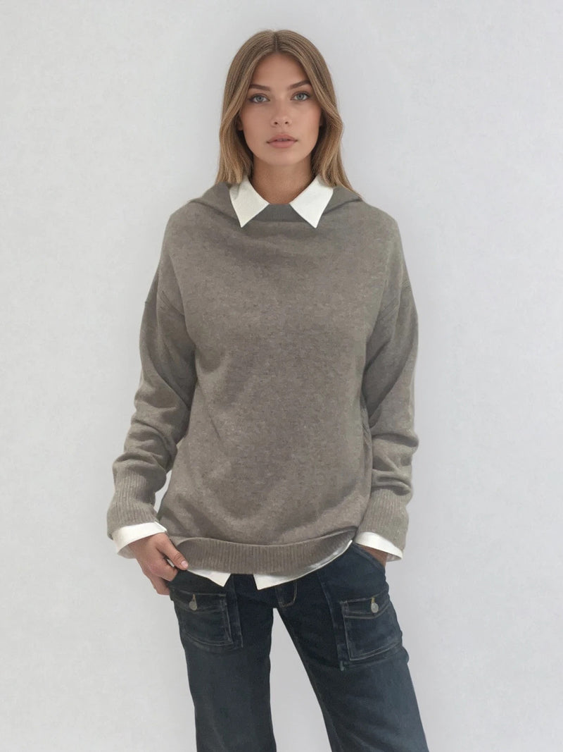 Pull taupe en 100% cachemire, manches longues avec une encolure ronde rehaussée d'une capuche. Coupe droite, esprit hoody, se porte assez vague. Les emmanchures sont basses. Un élégant travail de maille formé de 2 bandes termine chaque couture d'assemblage. Finitions côtes. Vue face.