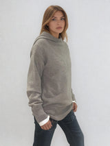 Pull taupe en 100% cachemire, manches longues avec une encolure ronde rehaussée d'une capuche. Coupe droite, esprit hoody, se porte assez vague. Les emmanchures sont basses. Un élégant travail de maille formé de 2 bandes termine chaque couture d'assemblage. Finitions côtes. Vue profil.