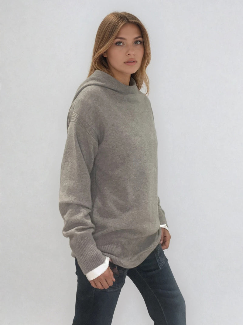 Pull taupe en 100% cachemire, manches longues avec une encolure ronde rehaussée d'une capuche. Coupe droite, esprit hoody, se porte assez vague. Les emmanchures sont basses. Un élégant travail de maille formé de 2 bandes termine chaque couture d'assemblage. Finitions côtes. Vue profil.