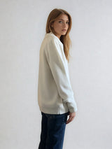 Pull polo écru en 42% cachemire, 8% soie, 50% mérinos. Le polo a un col large et ouvert avec 3 boutons. La coupe est droite et confort. Finitions côtes. Vue profil.