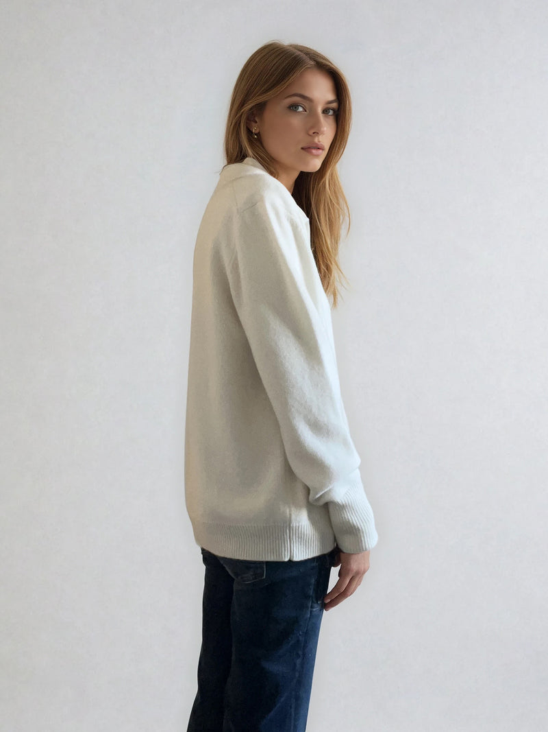Pull polo écru en 42% cachemire, 8% soie, 50% mérinos. Le polo a un col large et ouvert avec 3 boutons. La coupe est droite et confort. Finitions côtes. Vue profil.