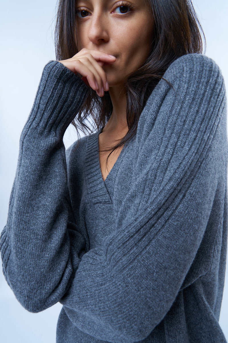 Robe pull manches longues grise avec un col V. Elle est longue et arrive aux mollets. Elle est fendue sur les côtés pour mieux se déplacer. Allure sport chic, confortable et chaude : 42% cachemire, 8% soie, 50% mérinos. Vue détail encolure V.