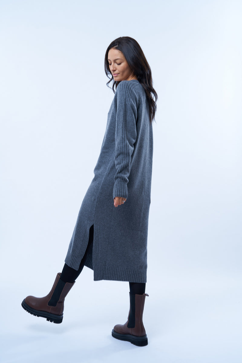 Robe pull manches longues grise avec un col V. Elle est longue et arrive aux mollets. Elle est fendue sur les côtés pour mieux se déplacer. Allure sport chic, confortable et chaude : 42% cachemire, 8% soie, 50% mérinos. Détail fente.