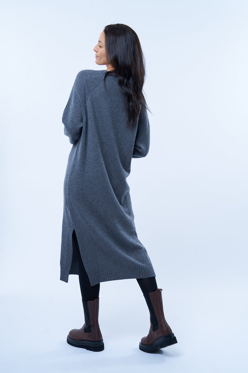 Robe pull manches longues grise avec un col V. Elle est longue et arrive aux mollets. Elle est fendue sur les côtés pour mieux se déplacer. Allure sport chic, confortable et chaude : 42% cachemire, 8% soie, 50% mérinos. Vue dos.