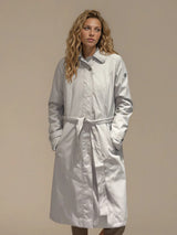 Trench beige 100% polyester avec une coupe droite, resserré par une ceinture. Longueur genoux. Fermeture avec zip et patte de boutonnage pressions. Vue face: trench ceinturé.