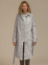 Trench beige 100% polyester avec une coupe droite, resserré par une ceinture. Longueur genoux. Fermeture avec zip et patte de boutonnage pressions. Vue face.