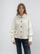Gilet en forme de blouson de coloris écru en cachemire, soie, et mérinos. La veste courte a une forme carrée, les emmanchures sont raglan. Le blouson a 2 poches poitrine, a un large col et est fermé de haut en bas par 5 boutons. Vue face.