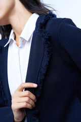 Veste manches longues marine en cachemire, laine et mérinos. La veste est bordée tout le long du col tailleur et en bas de petites franges marines en laine, se ferme avec 1 bouton et a  2 fausses poches sur les côtés. Coupe droite. Vue détail franges sur le col tailleur.